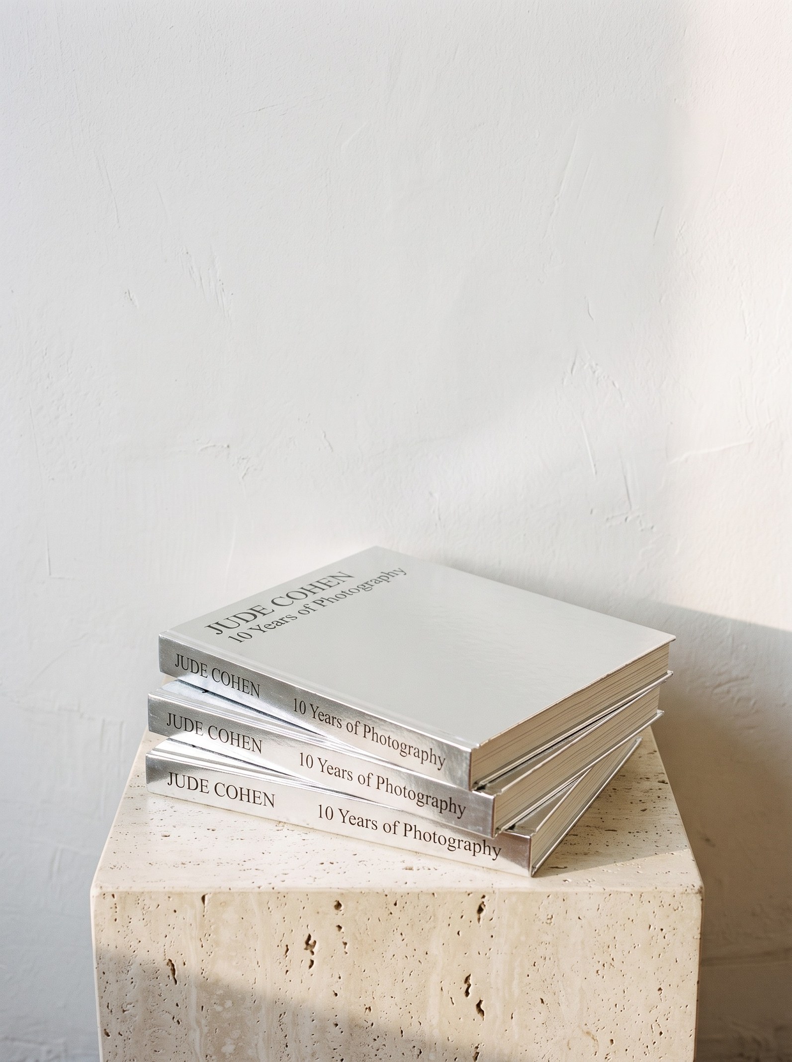 Three copies of Jude Cohen, 10 Years of Photography, Limited Collector's Edition, stacked on a travertine plinth